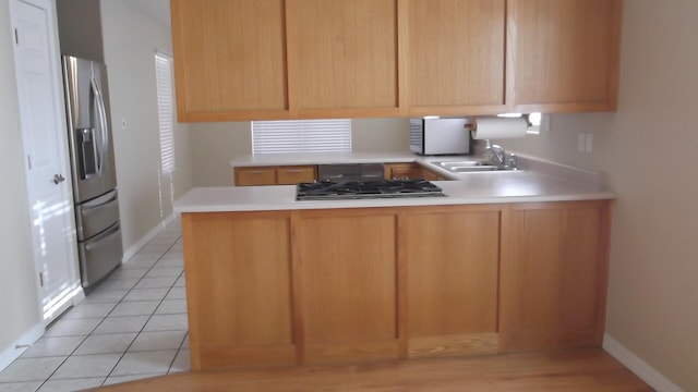 kitchen with black gas stovetop, kitchen peninsula, sink, light tile patterned floors, and stainless steel fridge with ice dispenser