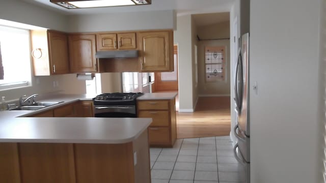 kitchen featuring kitchen peninsula, sink, light tile patterned flooring, black gas range oven, and stainless steel fridge