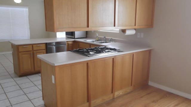 kitchen with light tile patterned flooring, sink, appliances with stainless steel finishes, kitchen peninsula, and light brown cabinetry