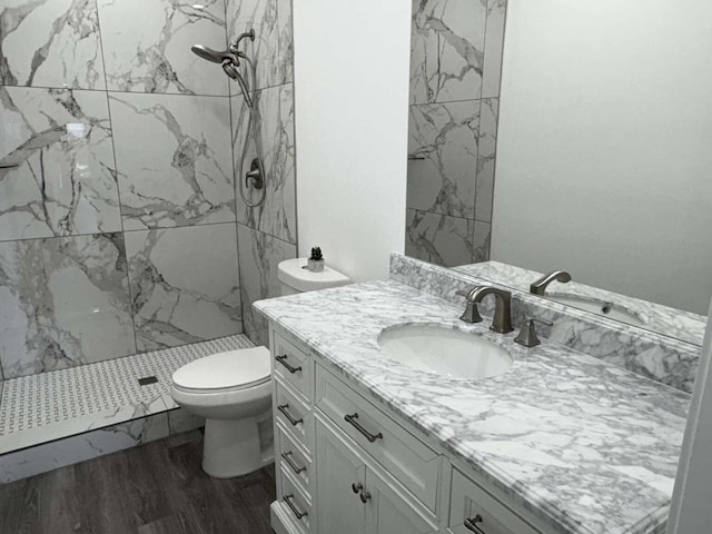 bathroom with a tile shower, vanity, wood-type flooring, and toilet