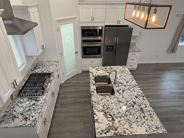 kitchen with light stone counters, range hood, pendant lighting, white cabinets, and appliances with stainless steel finishes