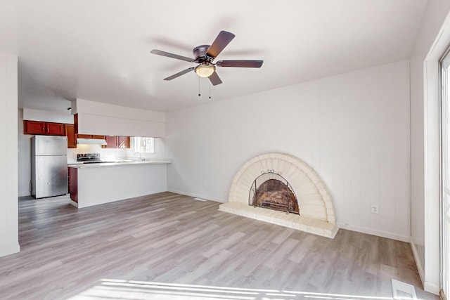 unfurnished living room with a brick fireplace, ceiling fan, sink, and light wood-type flooring