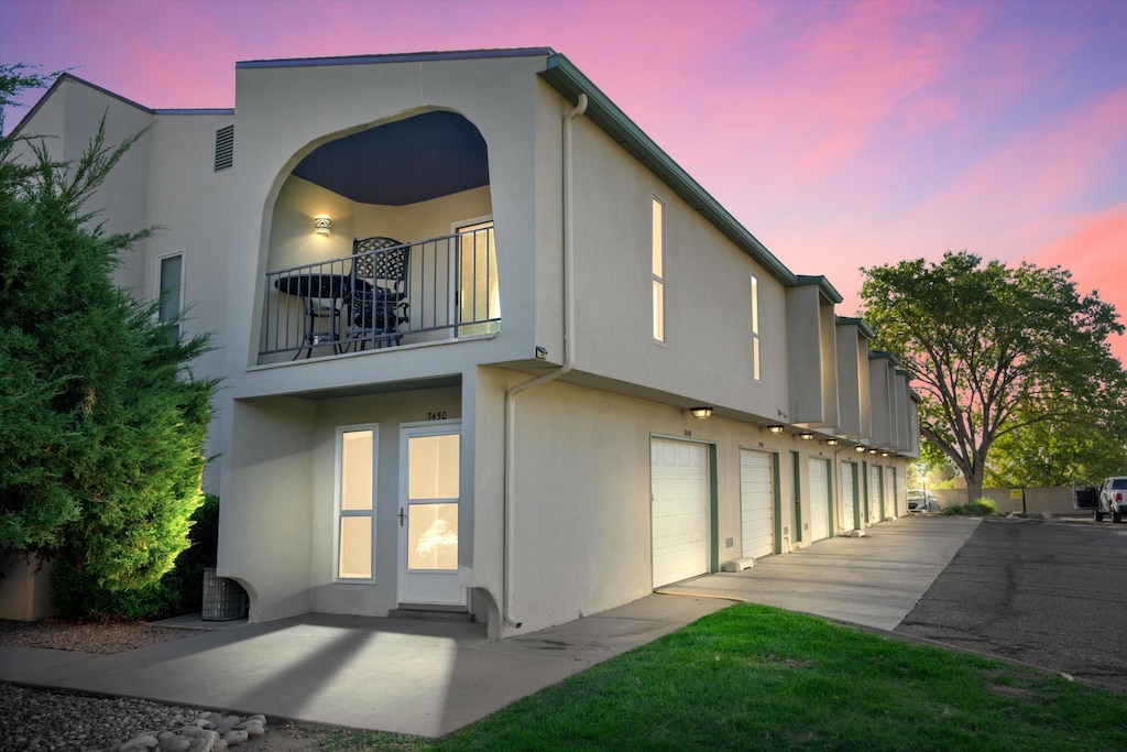 back house at dusk featuring a balcony and a garage