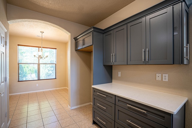 kitchen with light tile patterned floors, a textured ceiling, light stone countertops, a chandelier, and gray cabinetry