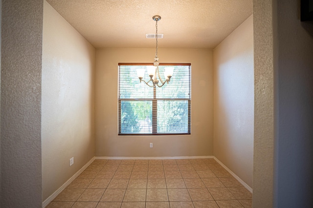 tiled spare room with a chandelier and a textured ceiling