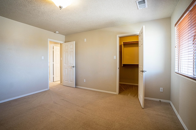 unfurnished bedroom featuring a textured ceiling, light carpet, a walk in closet, and a closet