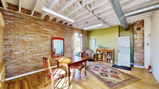 dining area with stacked washer / drying machine, wood-type flooring, and brick wall