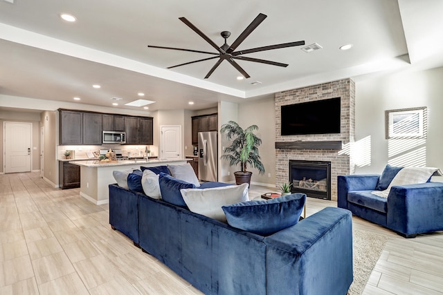 living room with ceiling fan, a raised ceiling, and a fireplace