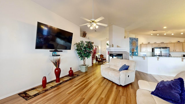 living room featuring high vaulted ceiling, a tiled fireplace, light hardwood / wood-style floors, and ceiling fan