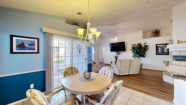 dining area featuring light hardwood / wood-style floors, a tiled fireplace, and ceiling fan with notable chandelier