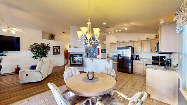 dining space featuring light hardwood / wood-style flooring, ceiling fan with notable chandelier, a fireplace, and vaulted ceiling