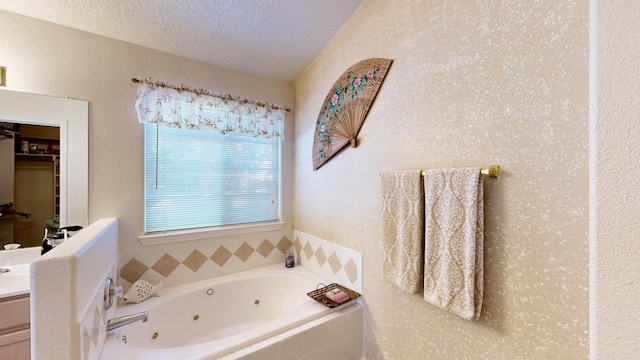 bathroom featuring vanity, a textured ceiling, and tiled tub