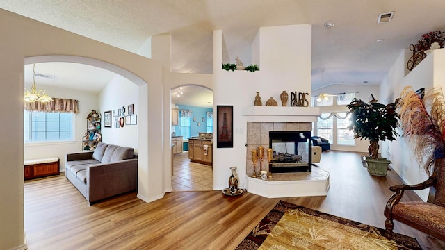 living room with a textured ceiling, lofted ceiling, light wood-type flooring, and a tile fireplace