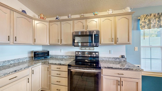 kitchen with light brown cabinetry, appliances with stainless steel finishes, a textured ceiling, and light stone counters