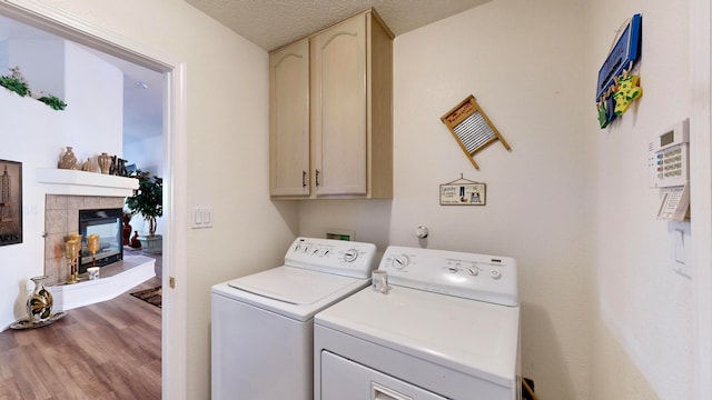 laundry area featuring washer and dryer, a textured ceiling, hardwood / wood-style floors, a tiled fireplace, and cabinets