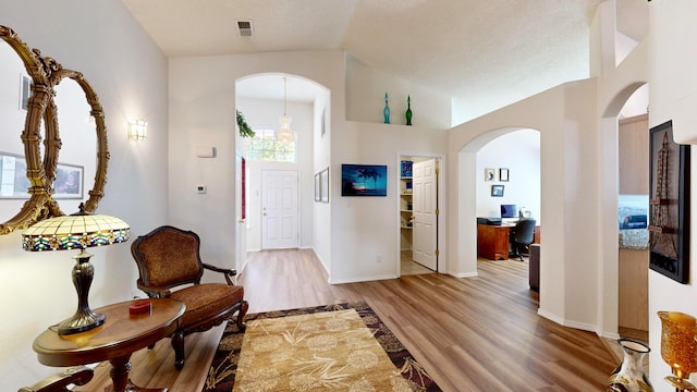 foyer entrance with a notable chandelier, light hardwood / wood-style floors, and high vaulted ceiling