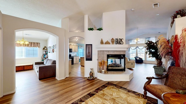 living room featuring lofted ceiling, light wood-type flooring, an inviting chandelier, and a tile fireplace