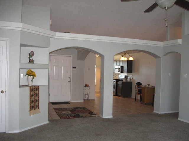 carpeted foyer entrance featuring a ceiling fan, arched walkways, tile patterned flooring, and a high ceiling