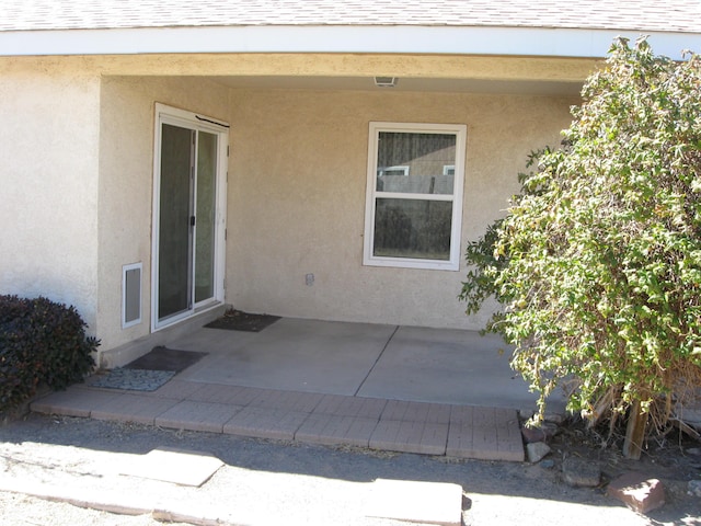 property entrance featuring a patio area, roof with shingles, and stucco siding