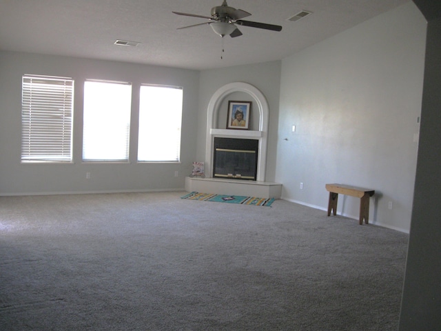 unfurnished living room with ceiling fan, carpet flooring, visible vents, baseboards, and a glass covered fireplace