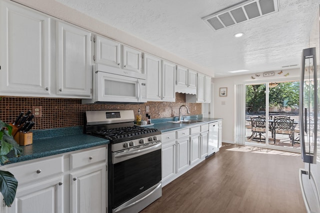 kitchen featuring dark countertops, visible vents, white cabinets, a sink, and white appliances