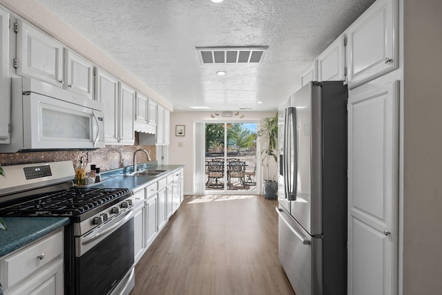 kitchen with a sink, visible vents, white cabinets, appliances with stainless steel finishes, and dark countertops