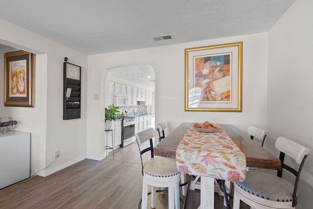 dining area with arched walkways, visible vents, light wood-style floors, a textured ceiling, and baseboards