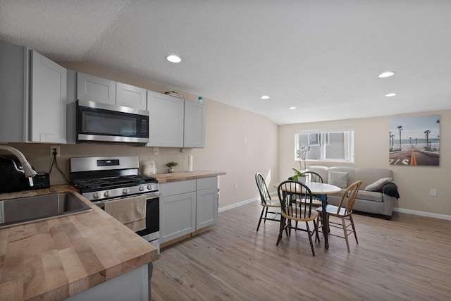 kitchen featuring stainless steel appliances, butcher block countertops, a sink, white cabinets, and open floor plan