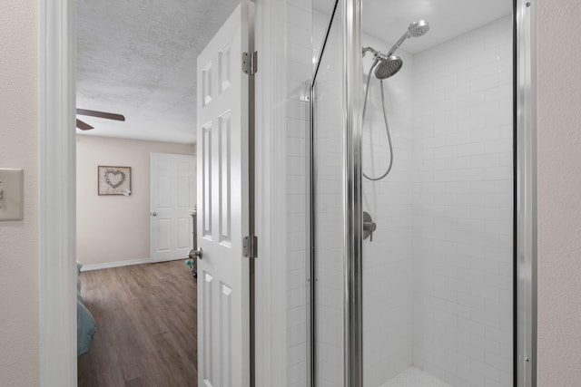 bathroom with a stall shower, baseboards, ceiling fan, wood finished floors, and a textured ceiling