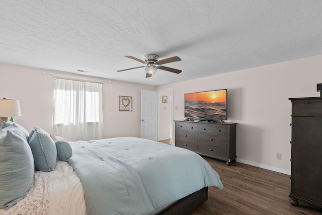 bedroom with a textured ceiling, a ceiling fan, visible vents, baseboards, and dark wood-style floors