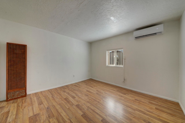 spare room featuring a wall mounted AC, light hardwood / wood-style flooring, and a textured ceiling