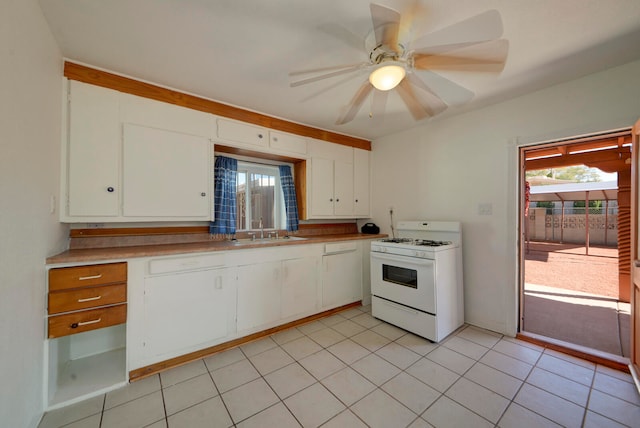 kitchen with ceiling fan, light tile patterned floors, white cabinetry, gas range gas stove, and sink