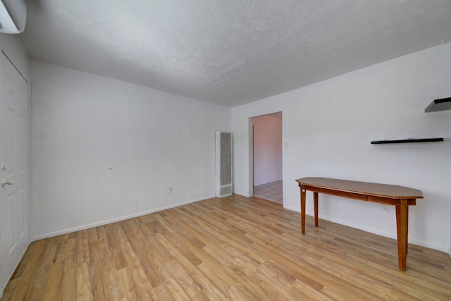 empty room featuring light hardwood / wood-style floors, a textured ceiling, and a wall mounted air conditioner