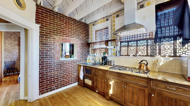 kitchen featuring light wood finished floors, brick wall, stainless steel gas stovetop, and exhaust hood