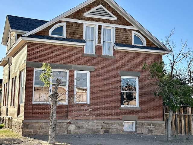 view of home's exterior featuring brick siding, roof with shingles, and fence