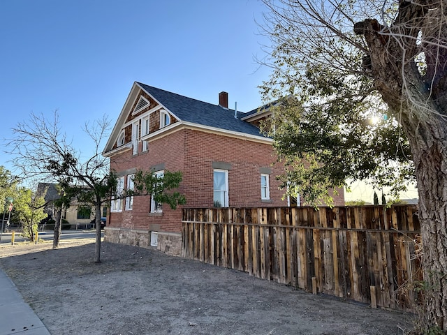 view of property exterior with brick siding, fence, and a chimney