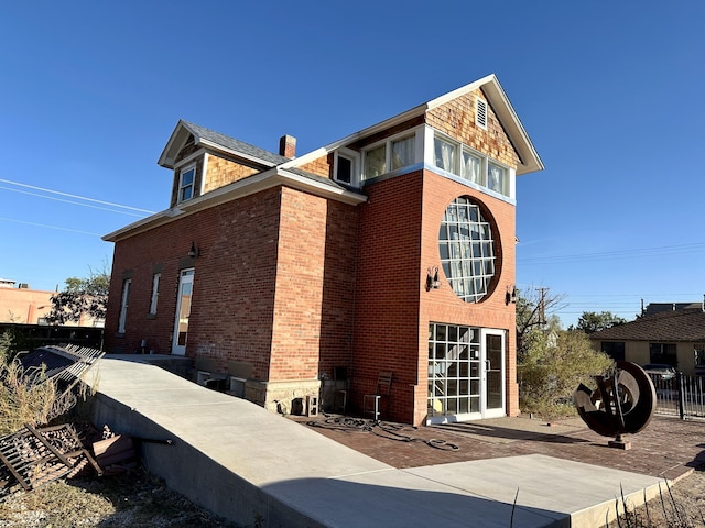 view of side of home with brick siding, fence, and a chimney