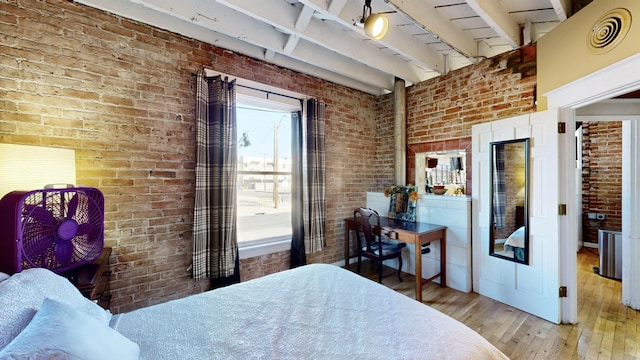 bedroom with beam ceiling, visible vents, hardwood / wood-style floors, and brick wall