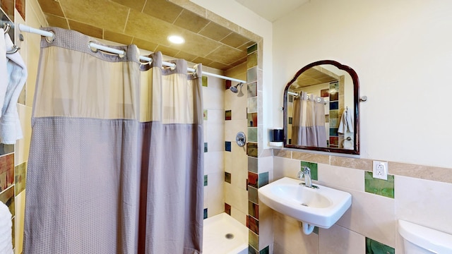 full bath with toilet, a stall shower, a sink, and tile walls