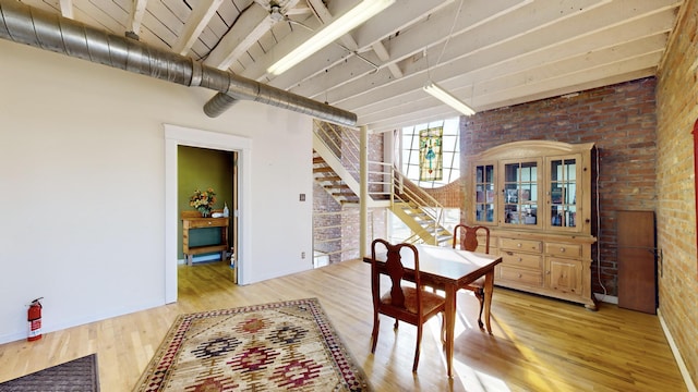 dining area with a high ceiling, brick wall, light wood-type flooring, baseboards, and stairs