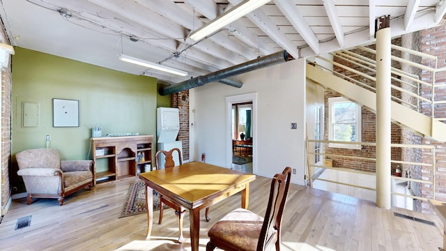 dining space featuring stacked washer and clothes dryer, light wood finished floors, and brick wall