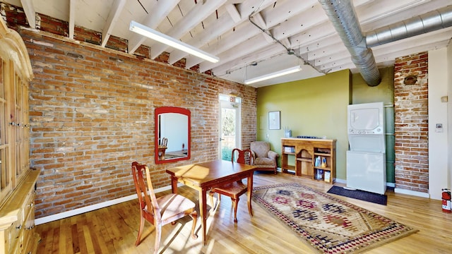 interior space with stacked washing maching and dryer, brick wall, beam ceiling, and wood finished floors