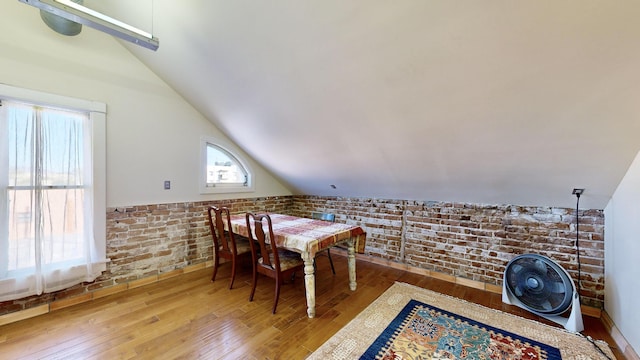 dining room with lofted ceiling, brick wall, and hardwood / wood-style flooring