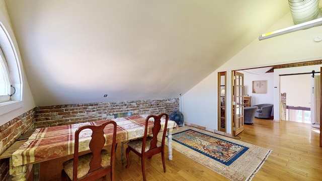 dining room featuring vaulted ceiling, brick wall, a barn door, and wood finished floors