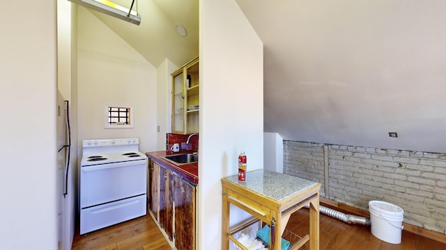 kitchen with brick wall, electric range, a sink, vaulted ceiling, and light wood-type flooring