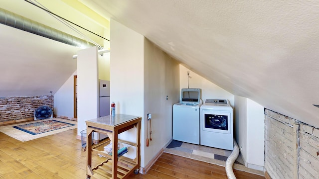 laundry room featuring washing machine and clothes dryer, a textured ceiling, brick wall, laundry area, and hardwood / wood-style flooring