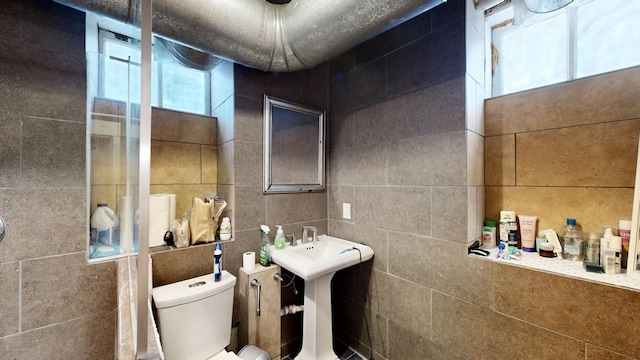 bathroom featuring a sink, toilet, and tile walls