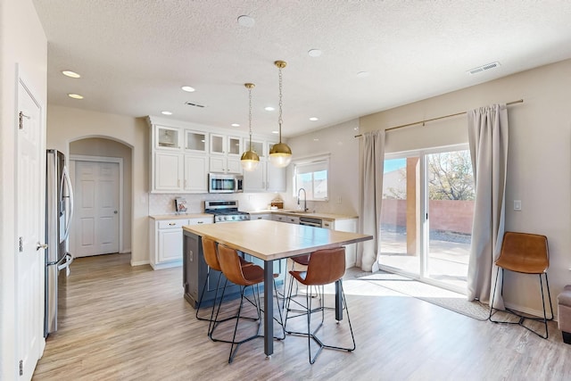 kitchen featuring appliances with stainless steel finishes, a center island, decorative light fixtures, white cabinets, and a breakfast bar area