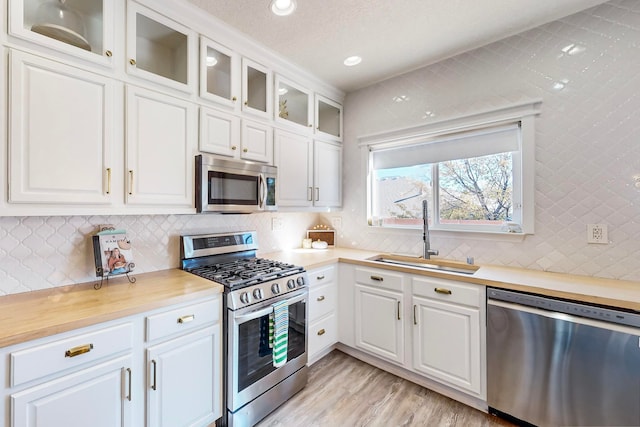 kitchen featuring tasteful backsplash, appliances with stainless steel finishes, sink, light hardwood / wood-style floors, and white cabinets