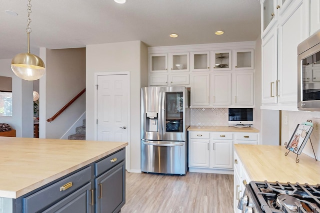 kitchen with decorative backsplash, light hardwood / wood-style flooring, hanging light fixtures, white cabinetry, and appliances with stainless steel finishes